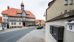A street view with a traditional half-timbered building, a clock tower, and a sign indicating a nearby restaurant.