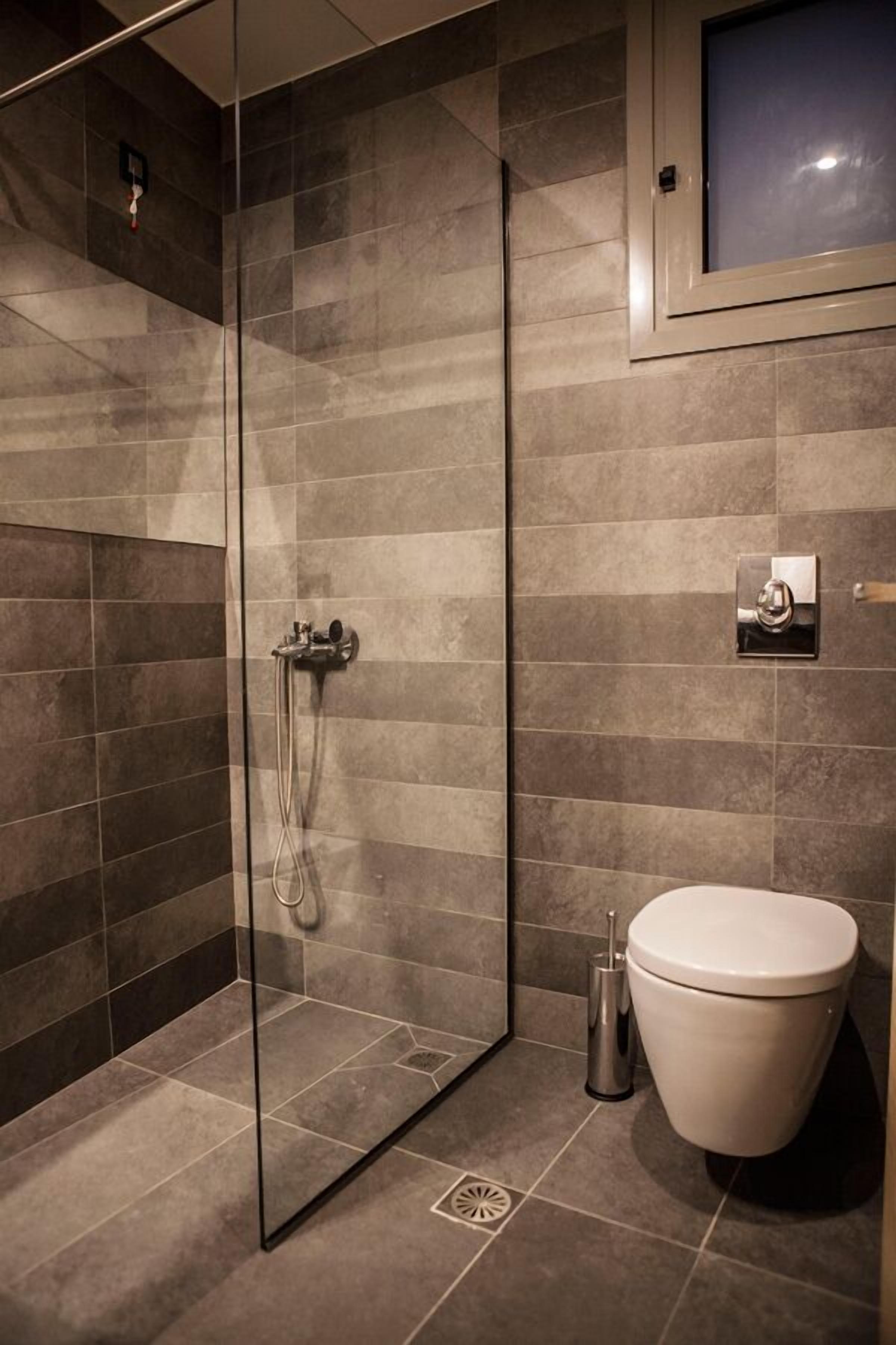 Un bany modern amb plat de dutxa envoltat de vidre, un vàter i un lavabo.