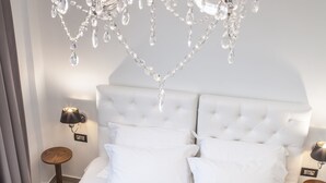 Un dormitorio con un cabecero blanco acolchado, una colcha gris con textura y una araña de cristal con cuatro luces que imitan velas.