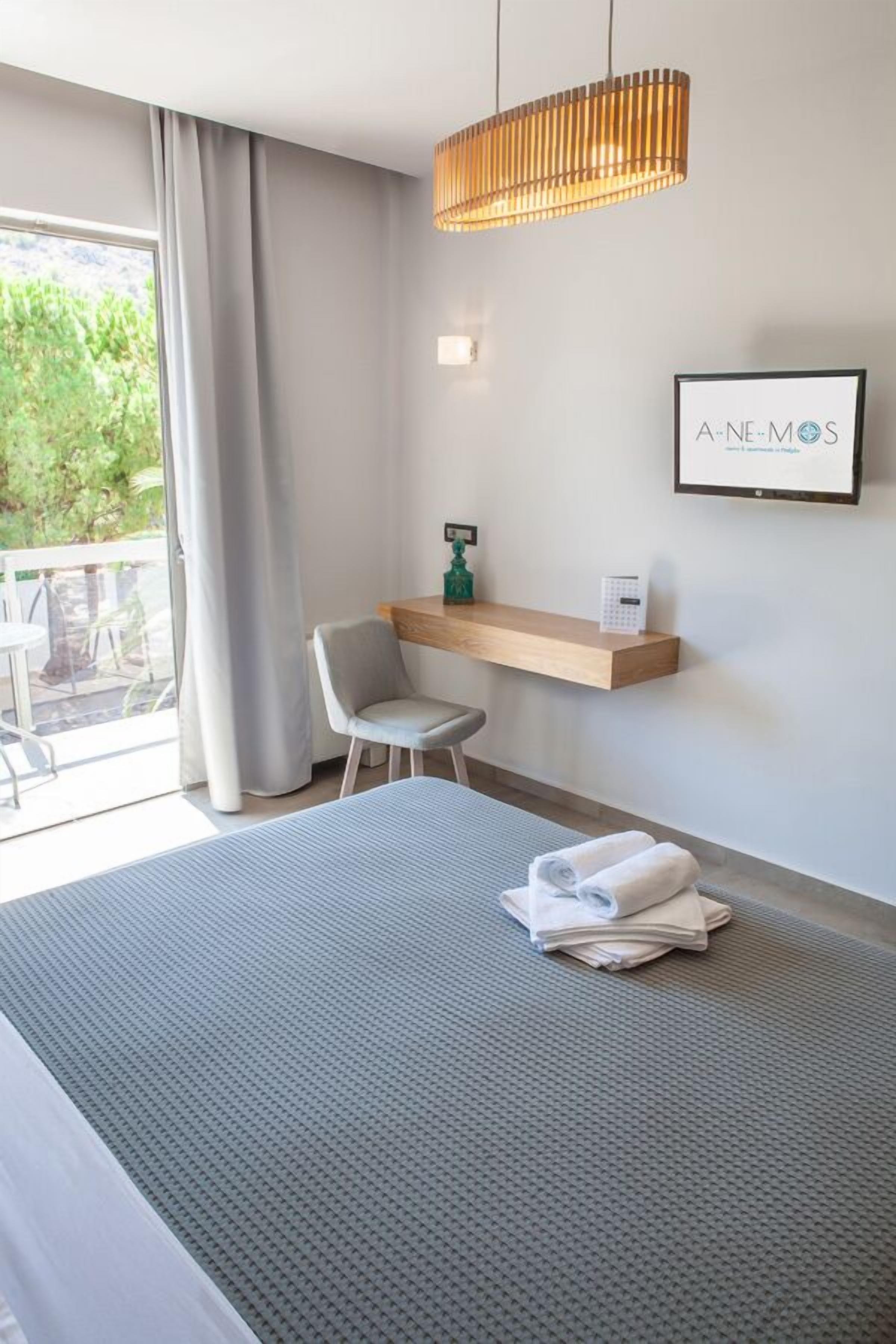 A modern hotel room with a bed, a desk, a chair, and a balcony with curtains.