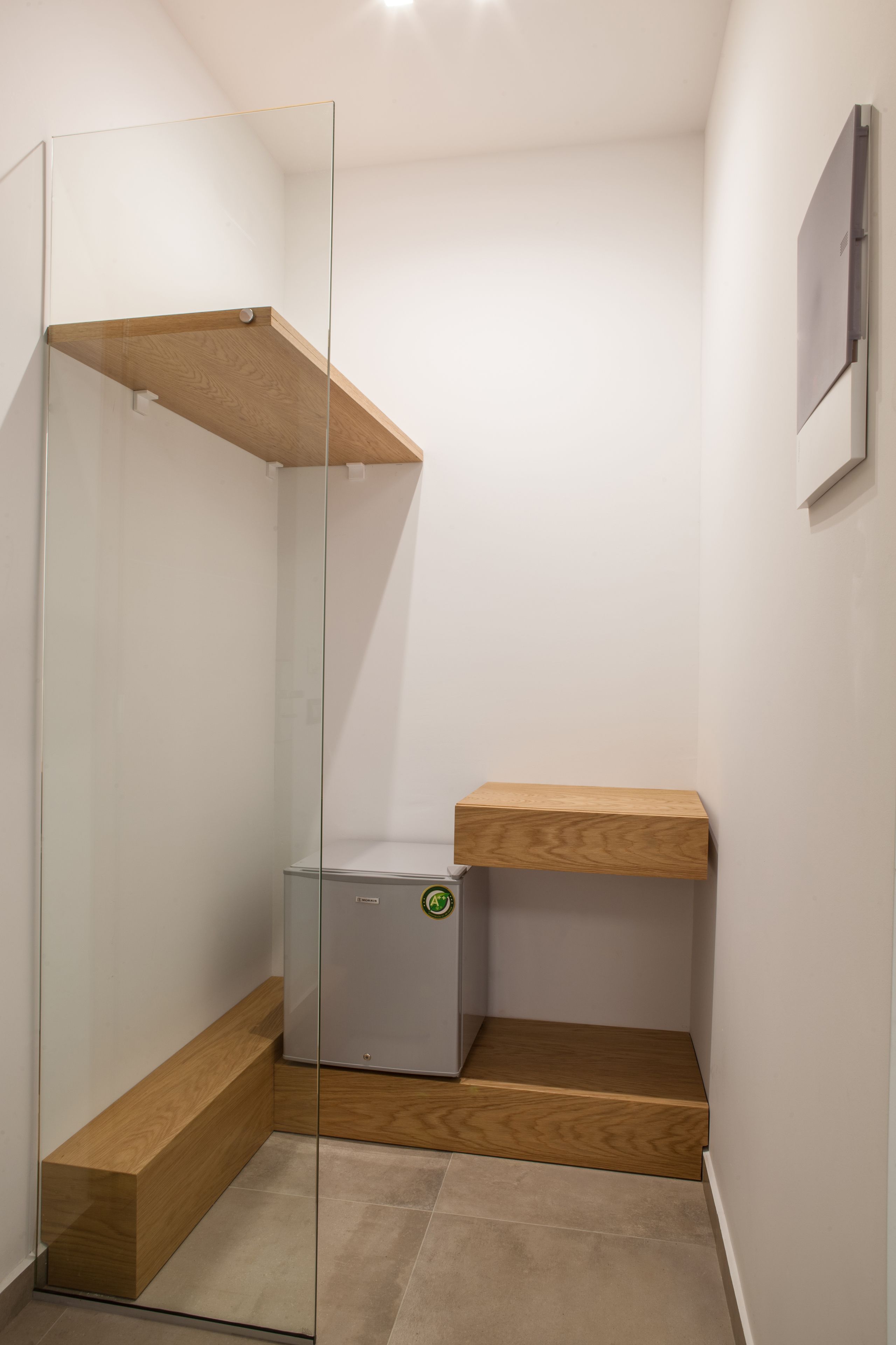 A corner of a room with a glass shower enclosure, a wooden bench, and a small gray cabinet.