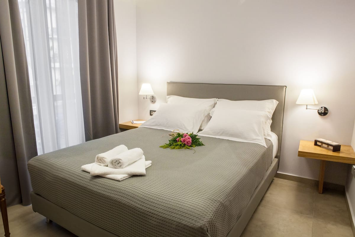 A neatly made bed with white linens and a floral arrangement, two bedside lamps, and a wooden nightstand with a remote control.