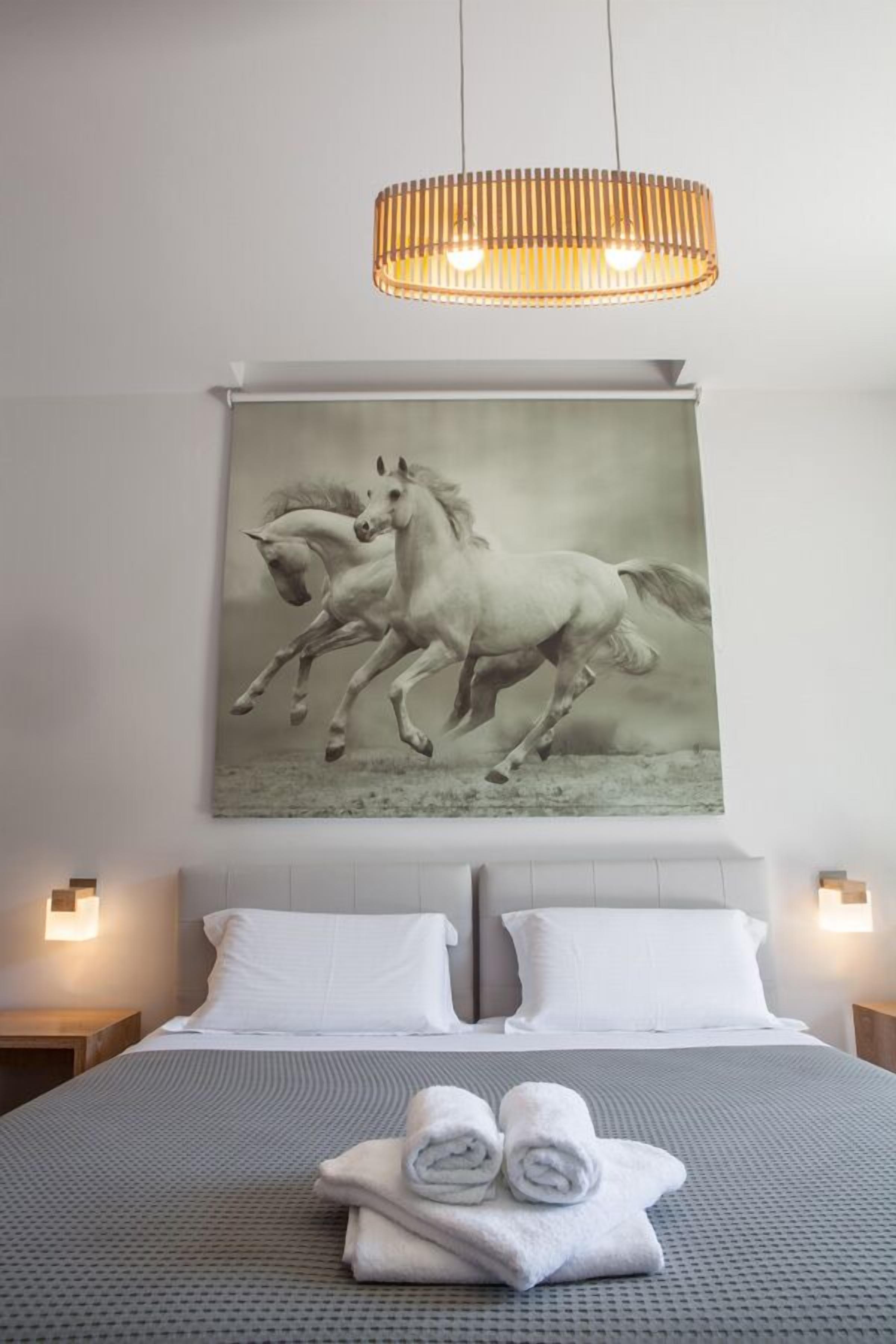 Habitación de hotel con una cama grande, dos mesitas de noche con lámparas, un cuadro de caballos en la pared y un aplique de techo.