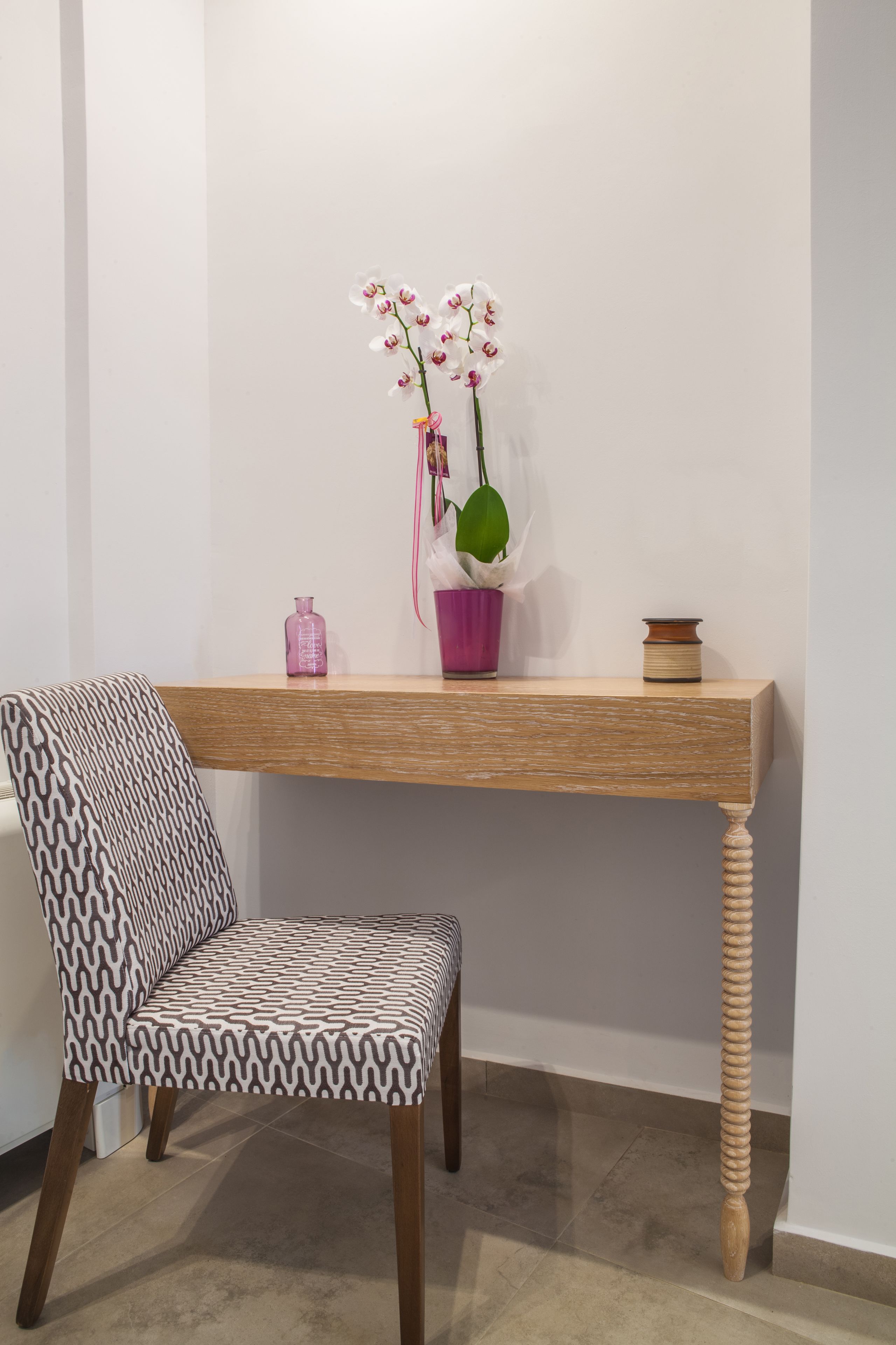 Een stoel met een gestreept zitkussen en een houten tafel met een vaas witte orchideeën en een kleine bloempot.