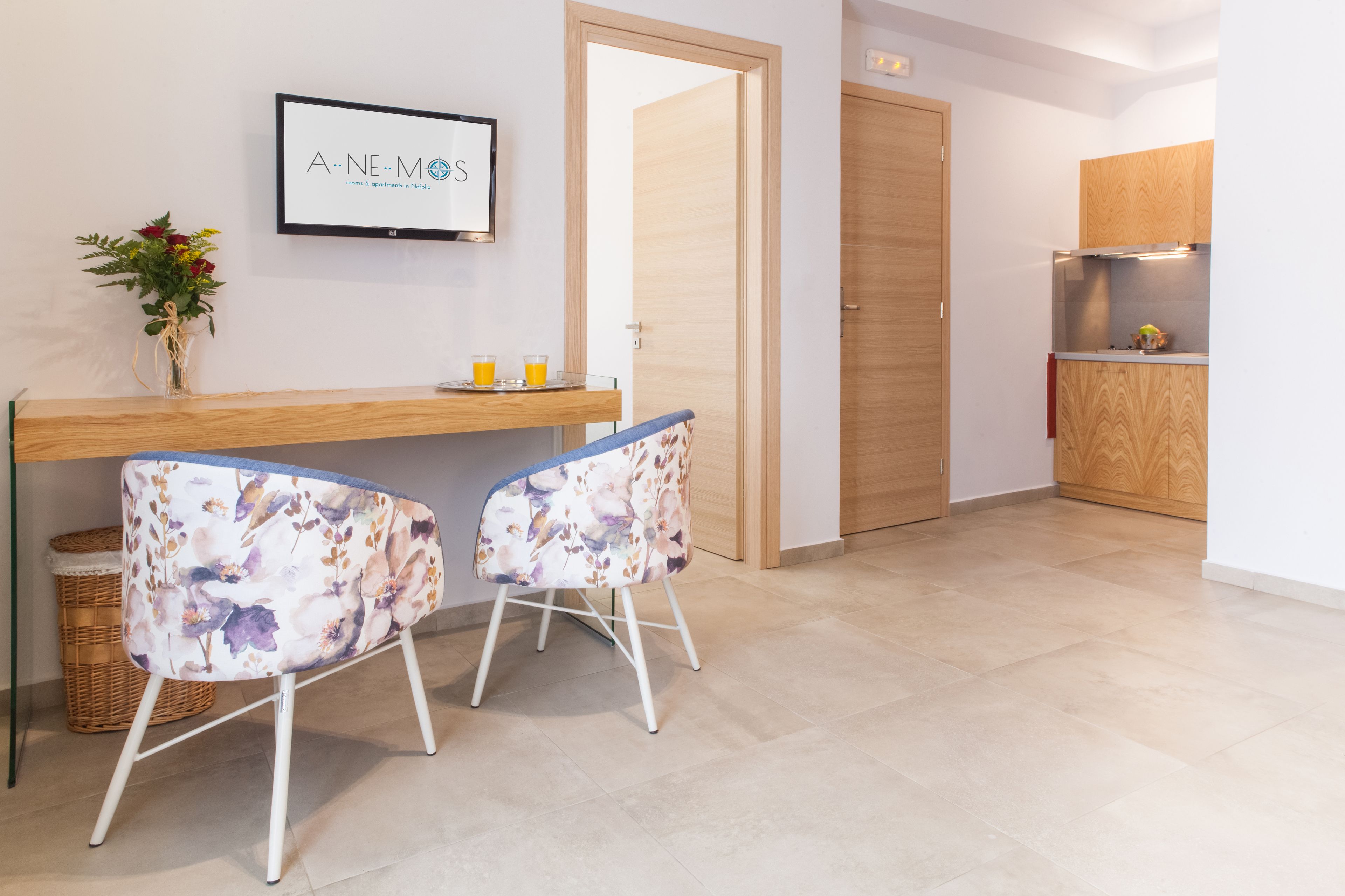 A modern kitchen with wooden cabinets, a built-in oven, and a small countertop. There are two chairs with floral upholstery and a wicker basket.
