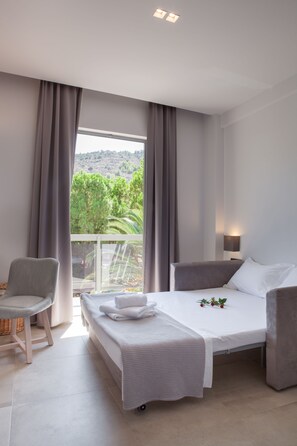 Quarto de hotel moderno com uma cama, uma cadeira, uma mesa de cabeceira e vista para o verde lá fora.