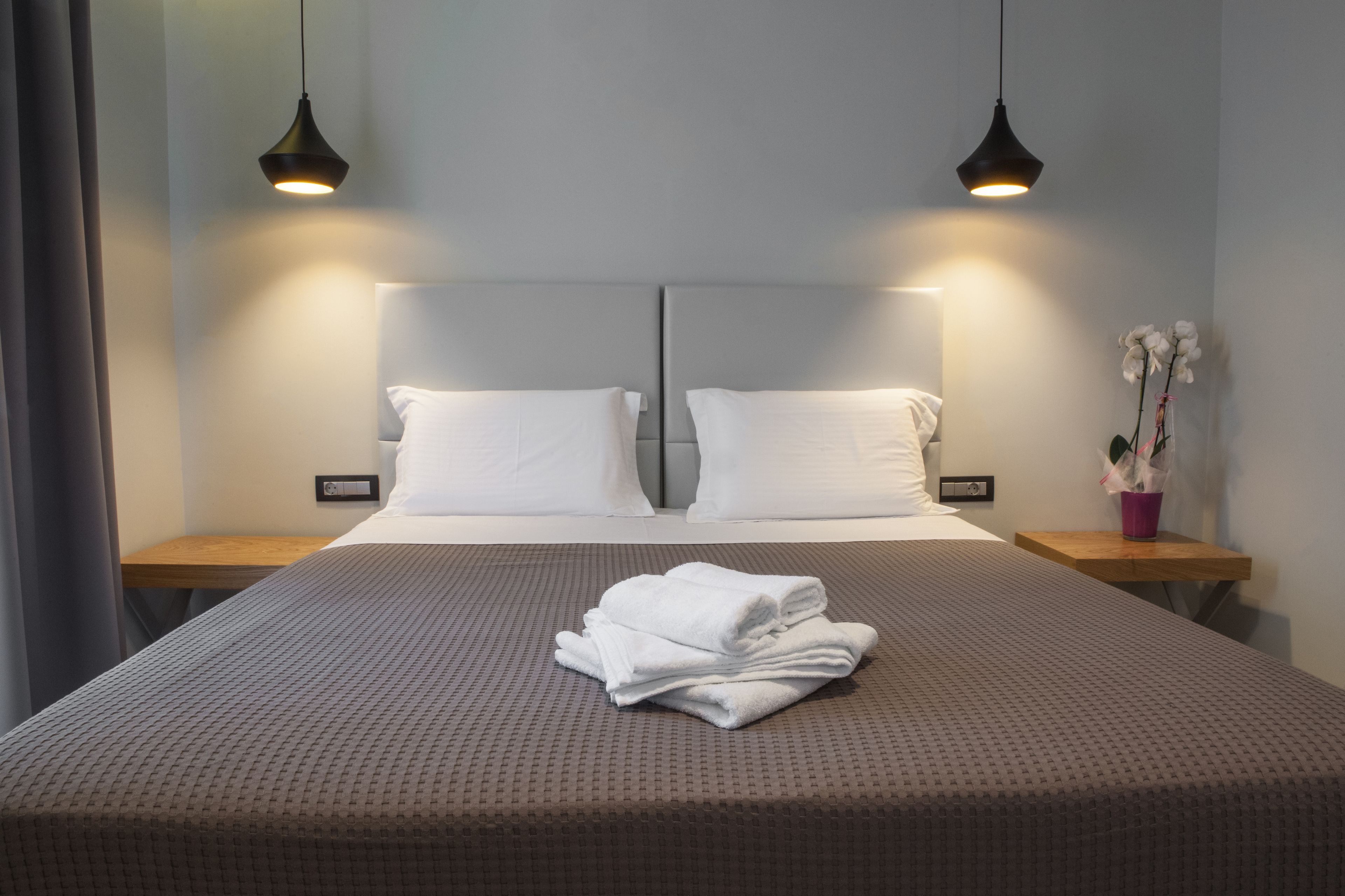 Ein ordentlich bezogenes Bett mit weißen Leinentüchern und einem gefalteten Handtuch, zwei Nachttische mit Lampen und eine kleine Topfpflanze auf einem Tisch.