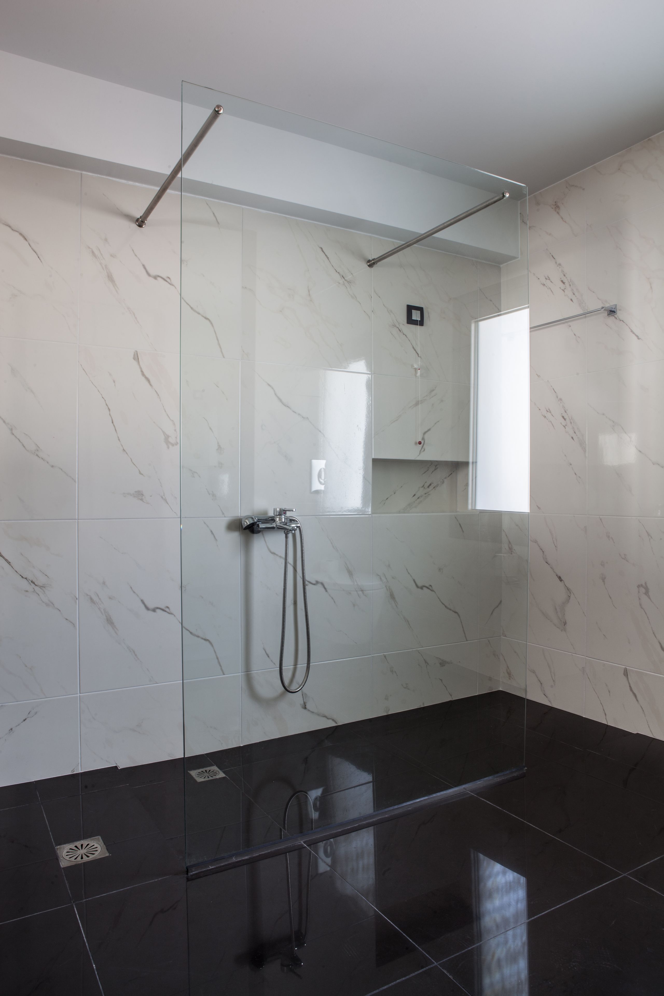 Un baño moderno con cabina de ducha de vidrio, paredes de mármol y suelo negro.