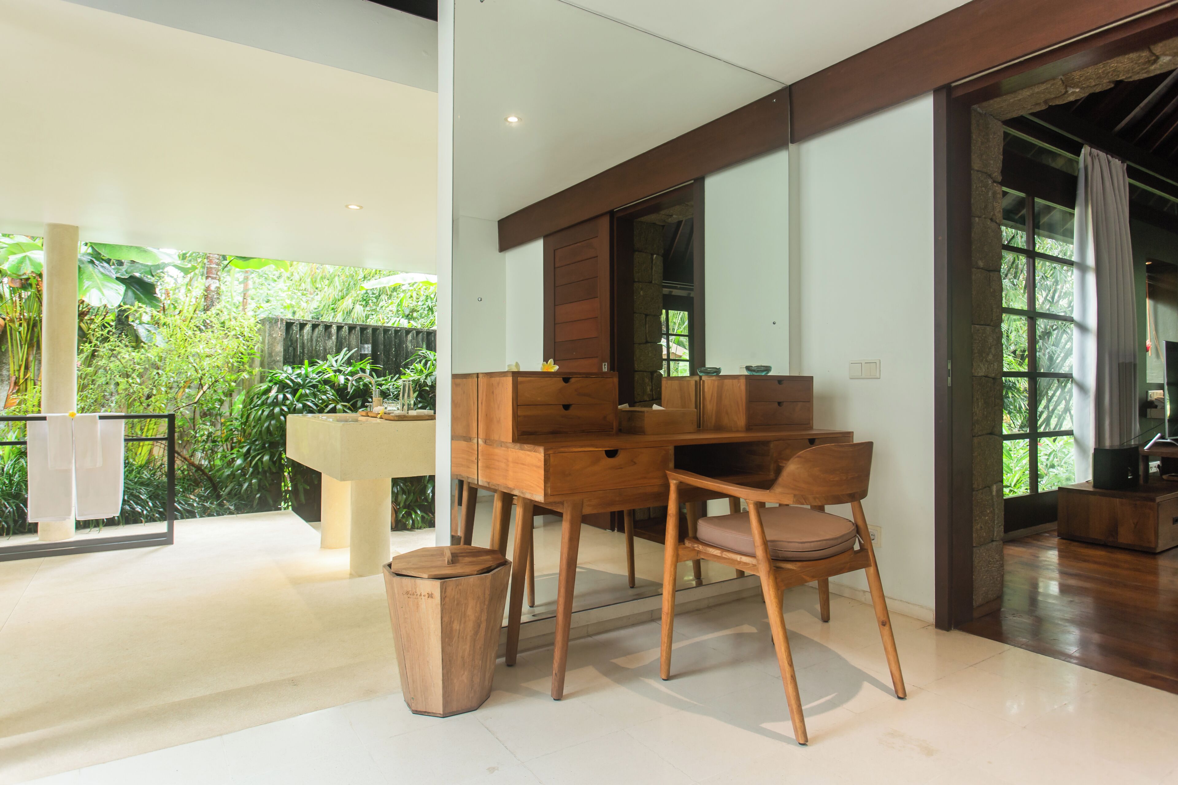 A modern room with a wooden desk, a chair, a small trash bin, and a large mirror.
