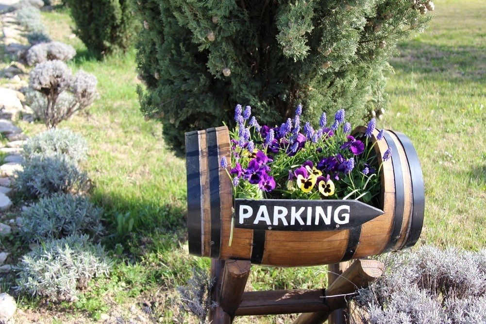 Een houten, trommelvormig bord met de tekst 'PARKING', buiten geplaatst met een tuin op de achtergrond.