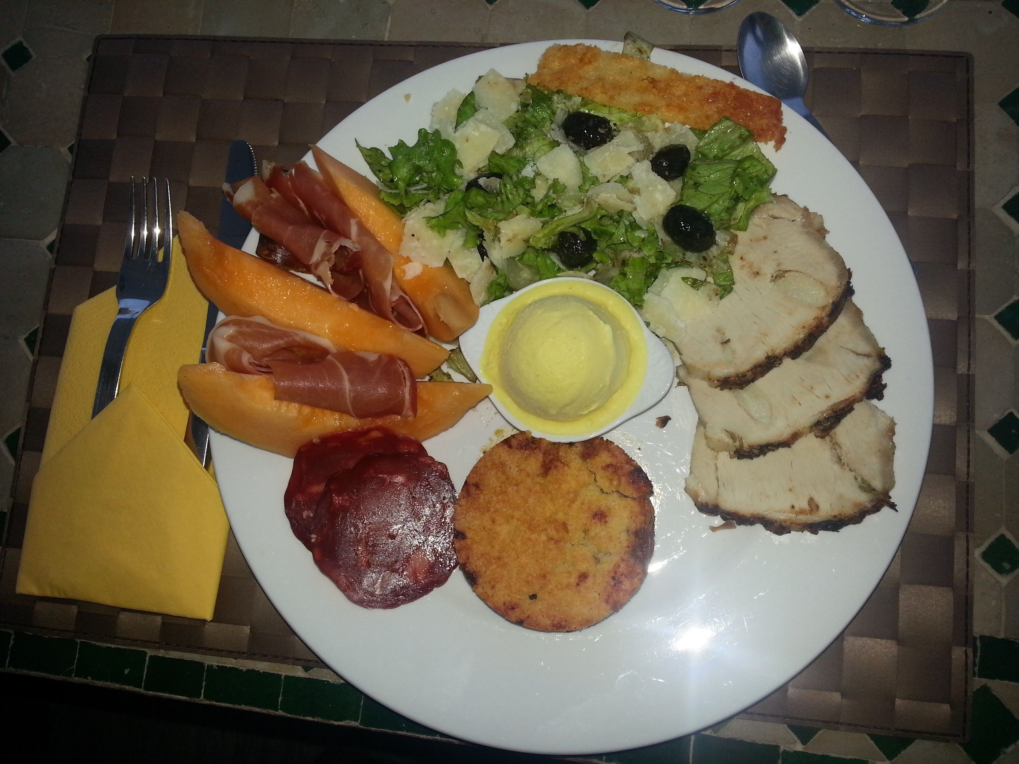 Une assiette de nourriture comprenant du jambon de Parme, du melon, de la salade et du pain.