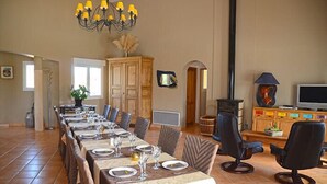 A dining area with a long table set for six, a chandelier, and a television in the background. - Villa des Cammaous (Vacquieres)