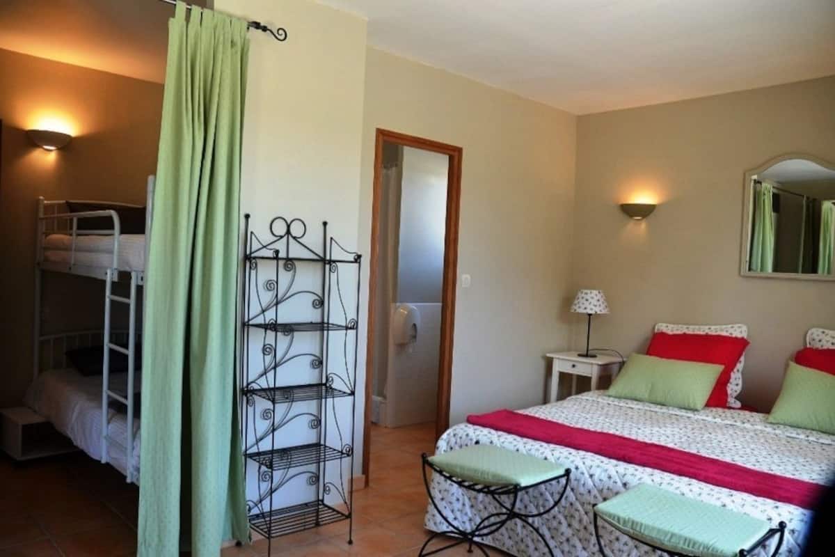 A bedroom with bunk beds, a metal shelf unit, a bedside table with a lamp, and a mirror on the wall.