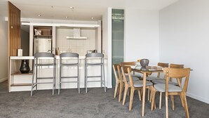 Une cuisine moderne avec des armoires blanches, un four encastré et un coin repas comprenant des chaises en bois et une table en verre.