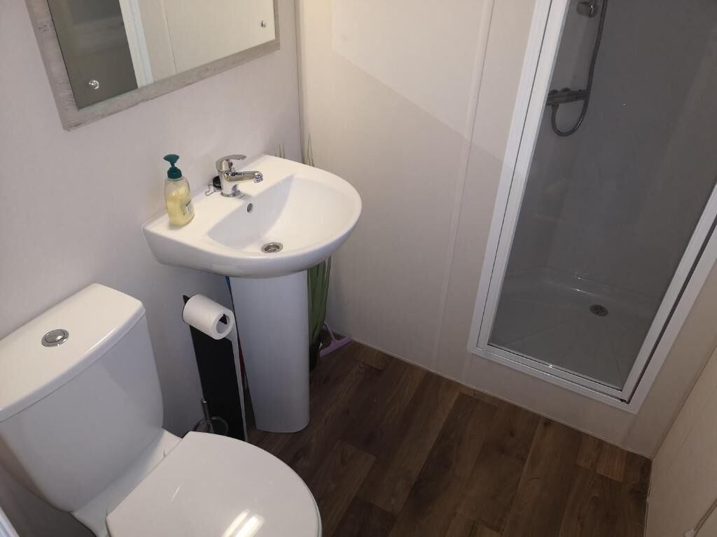 Une salle de bain avec des toilettes blanches, un lavabo avec un miroir au-dessus et un espace douche.
