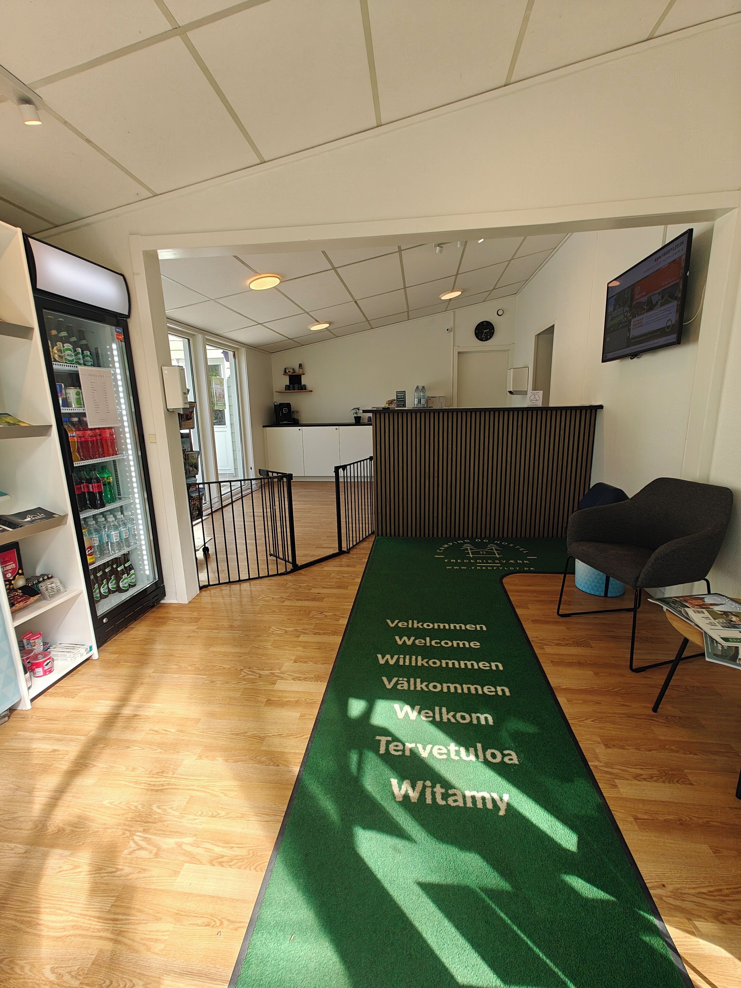 A reception area with a green welcome mat, a refrigerator stocked with beverages, and a seating area with a chair and a table.