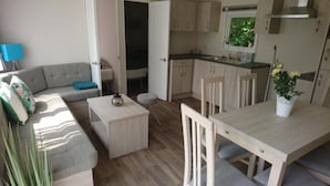 Un espacio habitable compacto con sofá, una mesita, una mesa de comedor con sillas, una zona de cocina y una puerta que da a otra habitación.