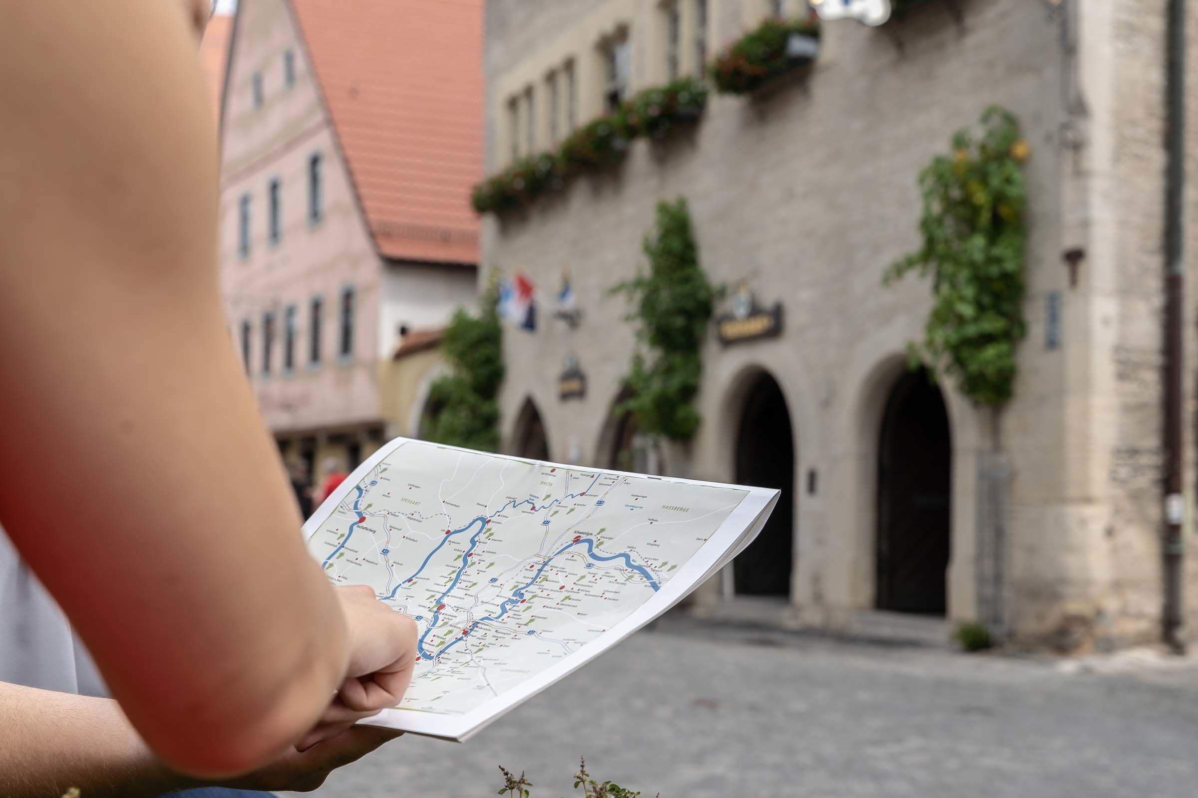 Uma pessoa segurando um mapa em frente a um edifício histórico com portas em arco e vegetação.