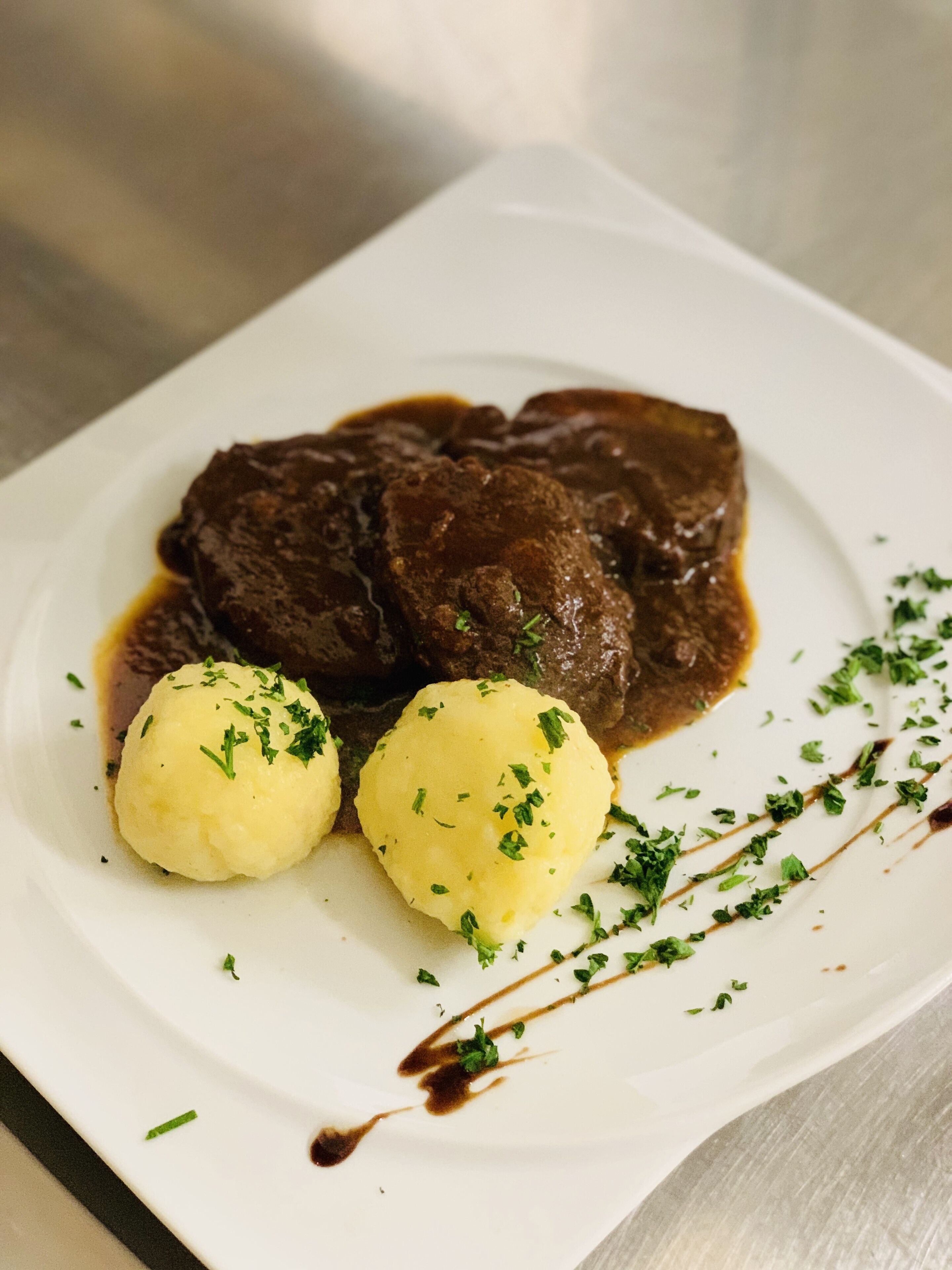 A plate with a beef dish and two dumplings, garnished with herbs.