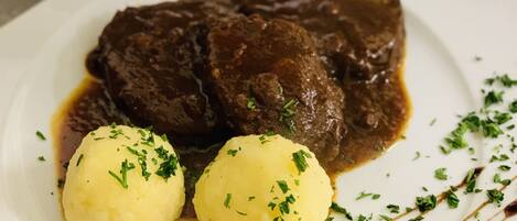 A plate with a beef dish and two dumplings, garnished with herbs.