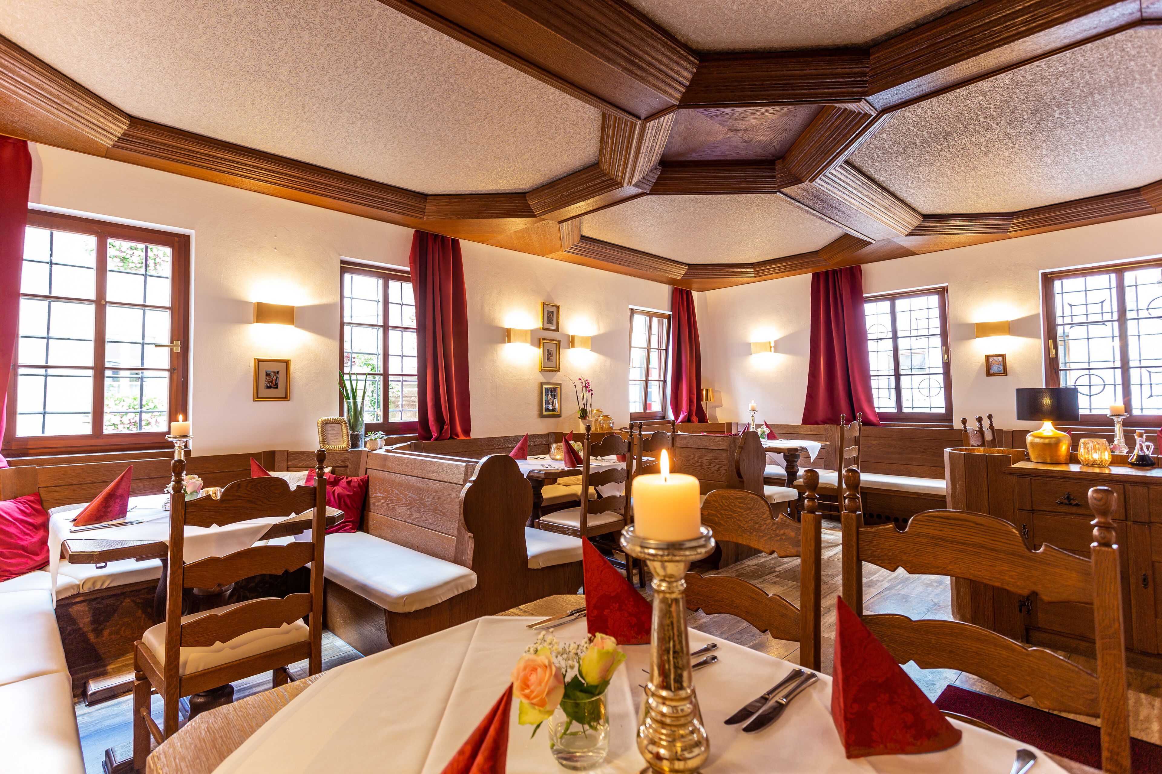 Un coin repas avec des meubles en bois, une table centrale agrémentée d’une bougie et des rideaux rouges.