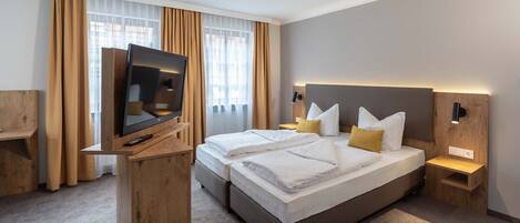 A modern hotel room with a large bed, a TV on a wooden stand, and a desk.