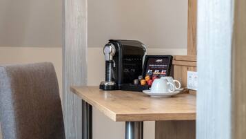 Una máquina de café, una taza y un menú sobre una mesa de madera en una habitación con una silla gris.