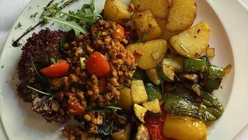 Un plato cuadrado blanco con diversos alimentos, incluyendo una hamburguesa, papas asadas y verduras mixtas.