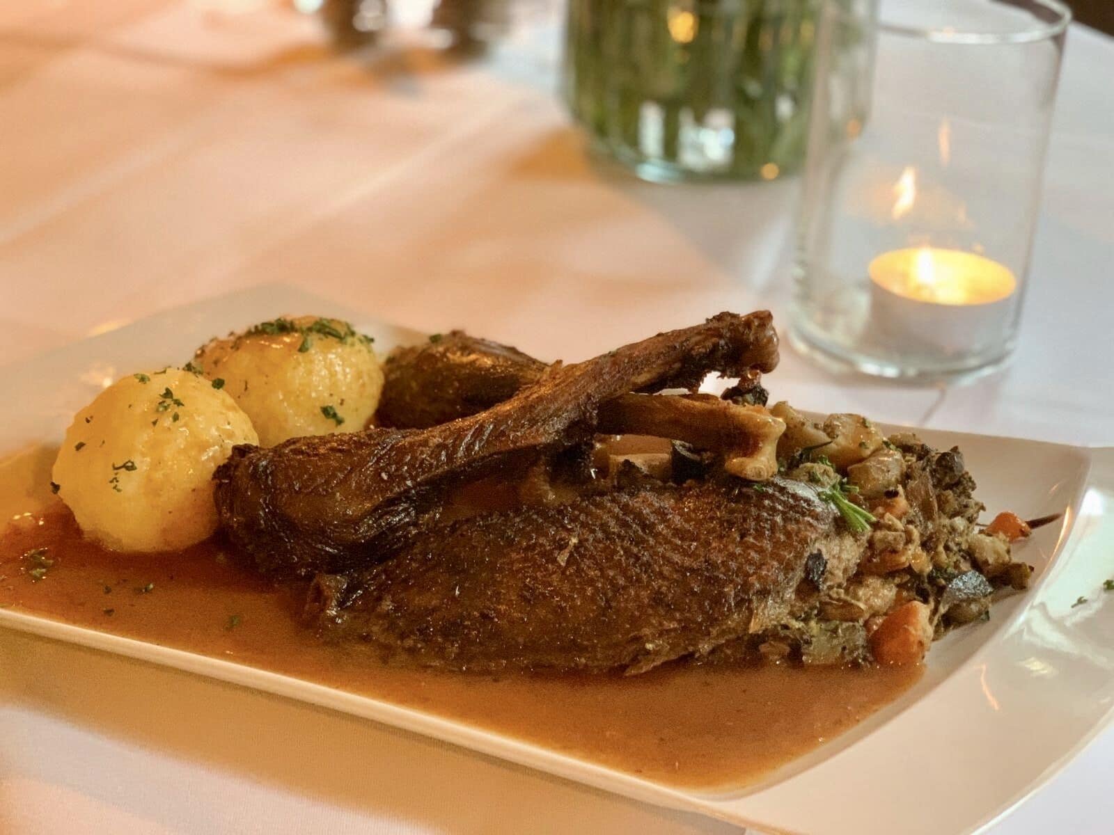 A plate of duck with sauce, potatoes, and vegetables.