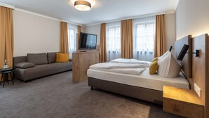 Hotellihuone, jossa on sänky, sohva, televisio ja puinen yöpöytä.