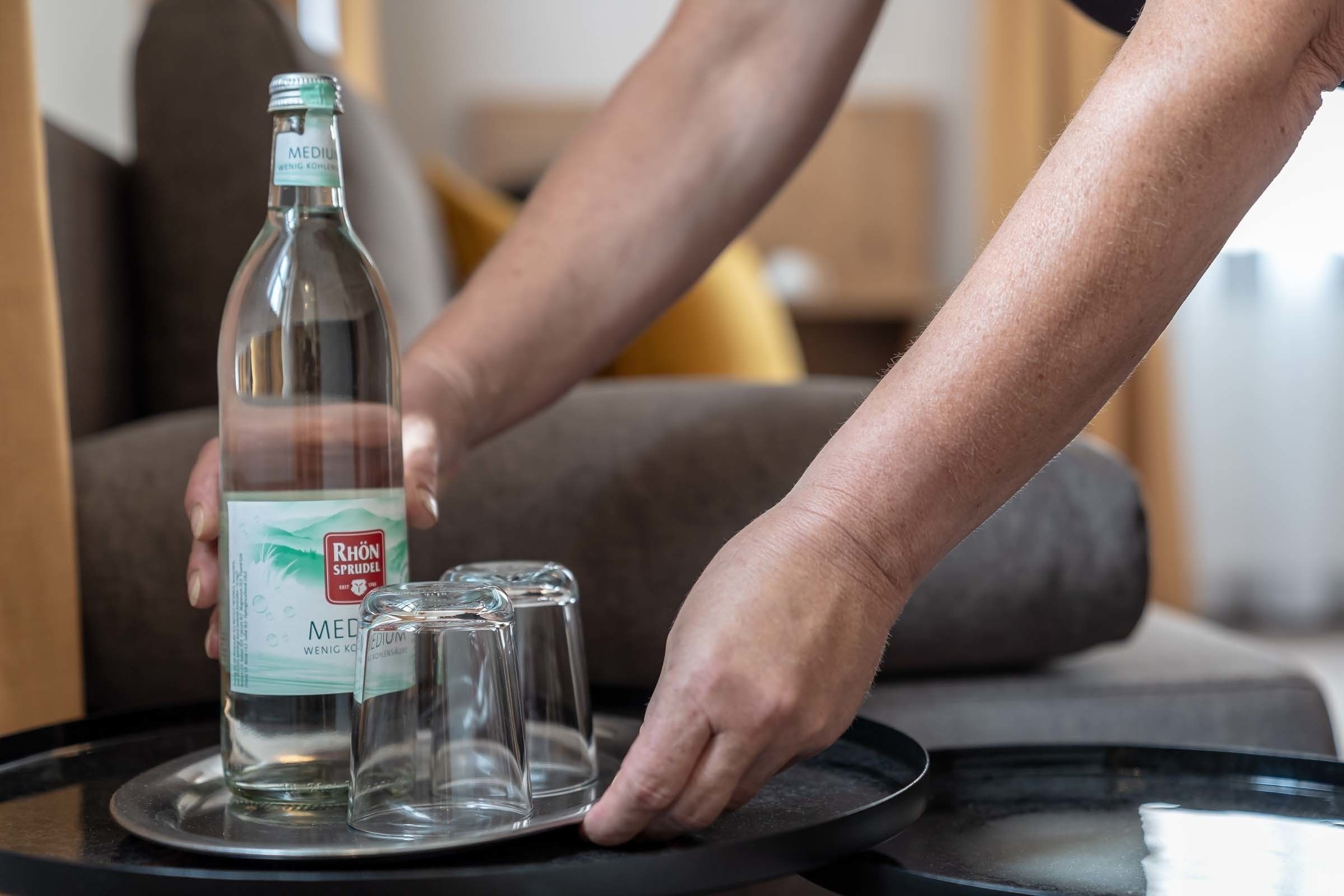 Una botella de Rhön Sprudel sobre una bandeja con dos vasos.