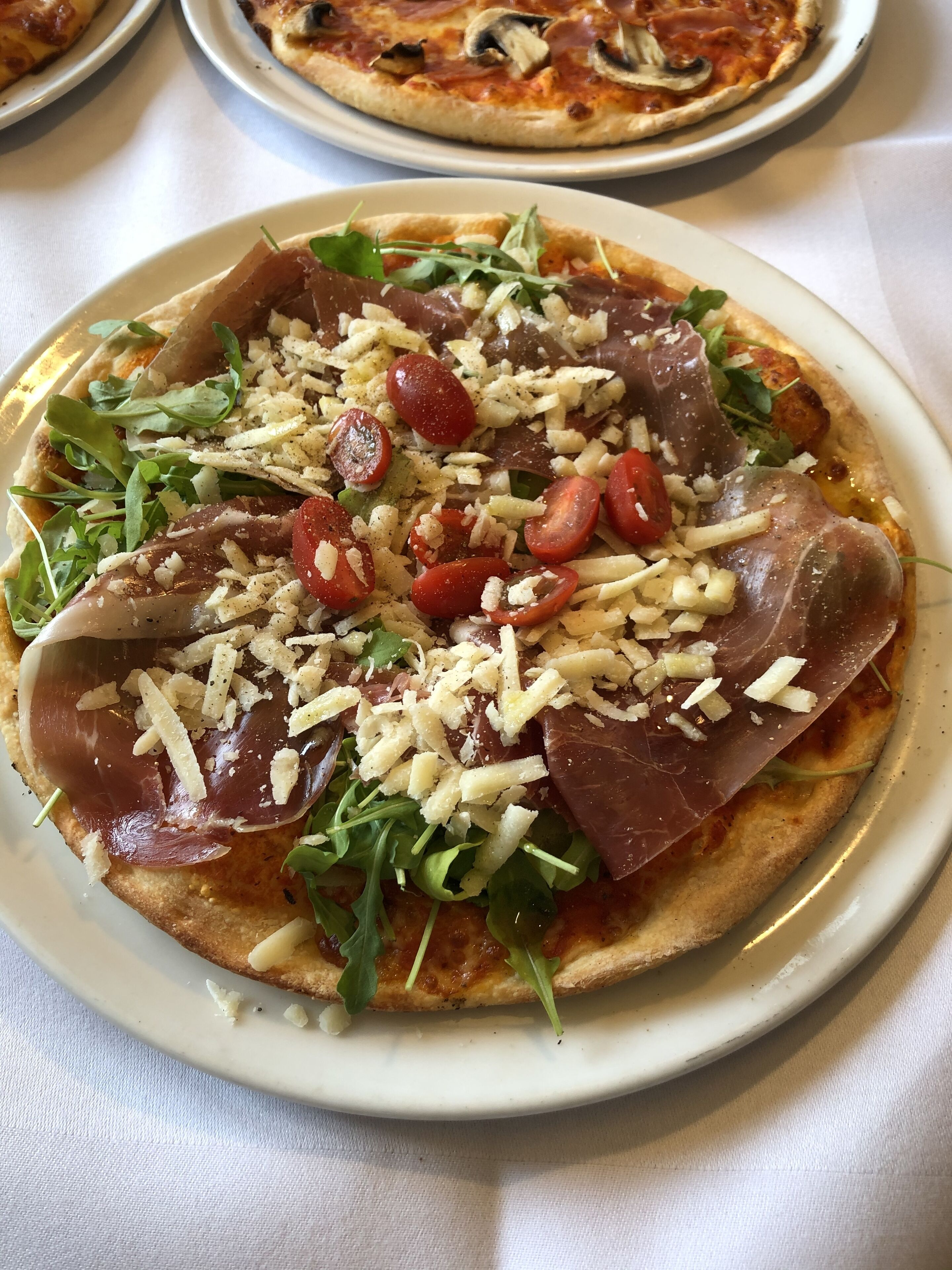 A pizza topped with arugula, cherry tomatoes, cheese, and prosciutto on a white plate.