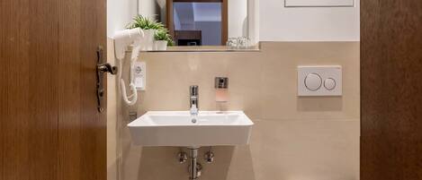 Un baño moderno con puerta de madera, un lavabo blanco, un espejo y un inodoro.