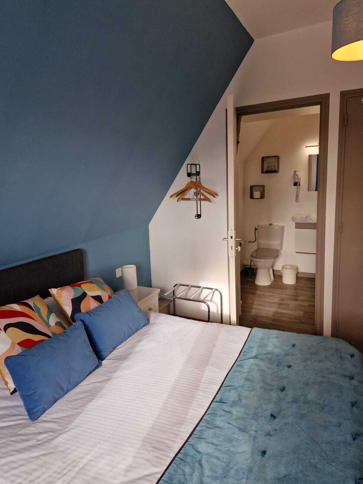 A bedroom with a bed, a bedside table, a hanging coat rack, and a view into the bathroom.
