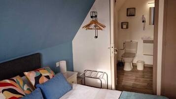 A bedroom with a bed, a bedside table, a hanging coat rack, and a view into the bathroom.