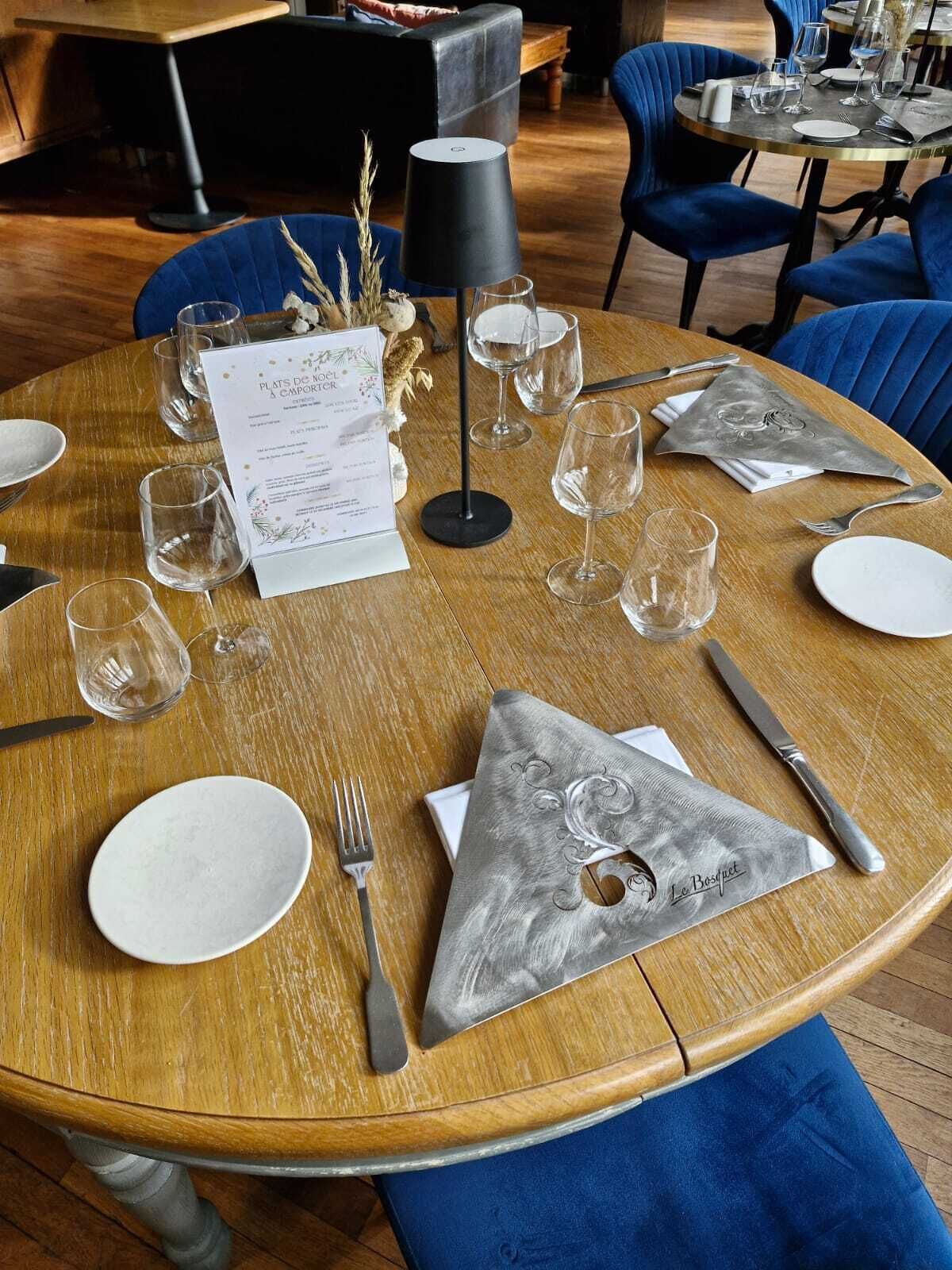 Een ronde eettafel is gedekt met witte borden, zilver bestek en glazen wijnglazen. Een menukaart ligt op tafel, en er staat een zwarte lamp.