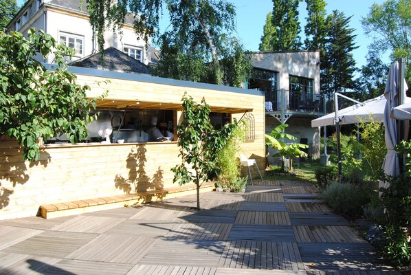 A wooden deck with a restaurant area, surrounded by greenery and trees.
