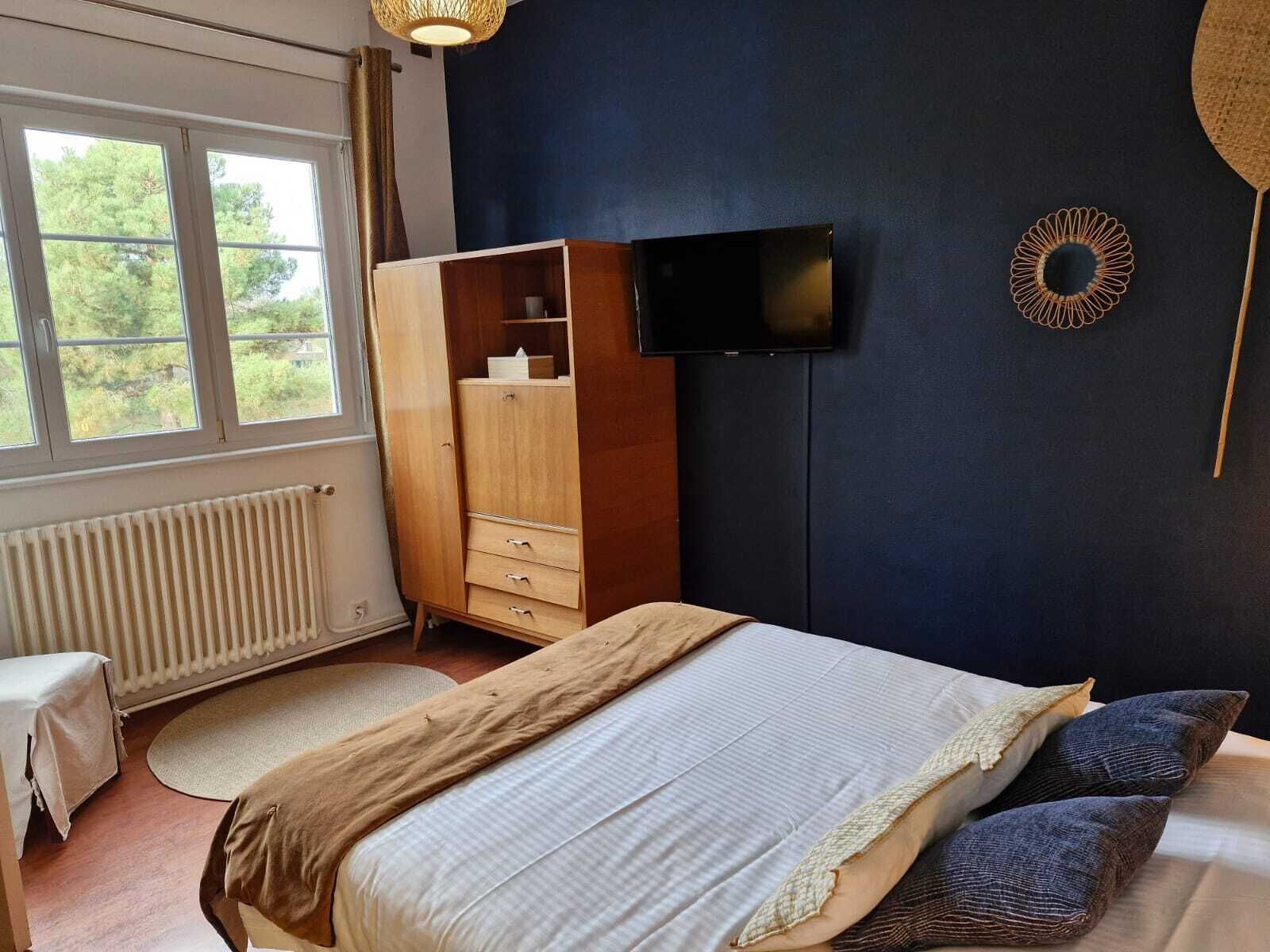Un dormitorio con cama, armario, televisor y vista a zonas verdes.