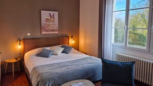 Une chambre à coucher avec un lit, des lampes de chevet, une petite table, une chaise et une fenêtre donnant sur des arbres.