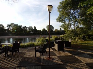 Ein Sitzbereich im Freien mit Stühlen und Tischen, einer Lampe und Blick auf einen See.