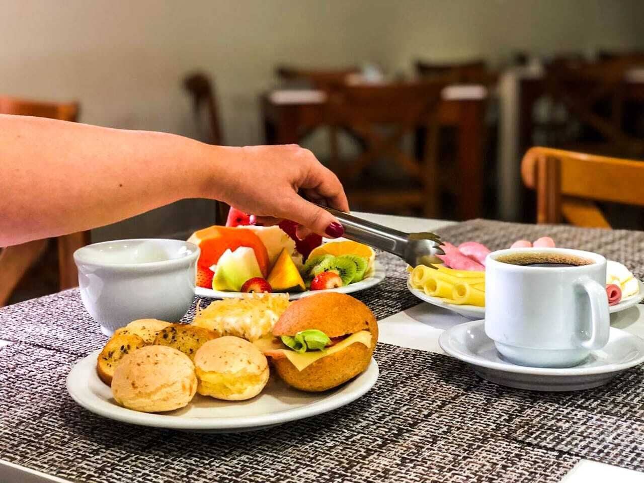 Et morgenbord med et udvalg af mad, blandt andet bagværk, en sandwich og frugt, samt en kop kaffe.
