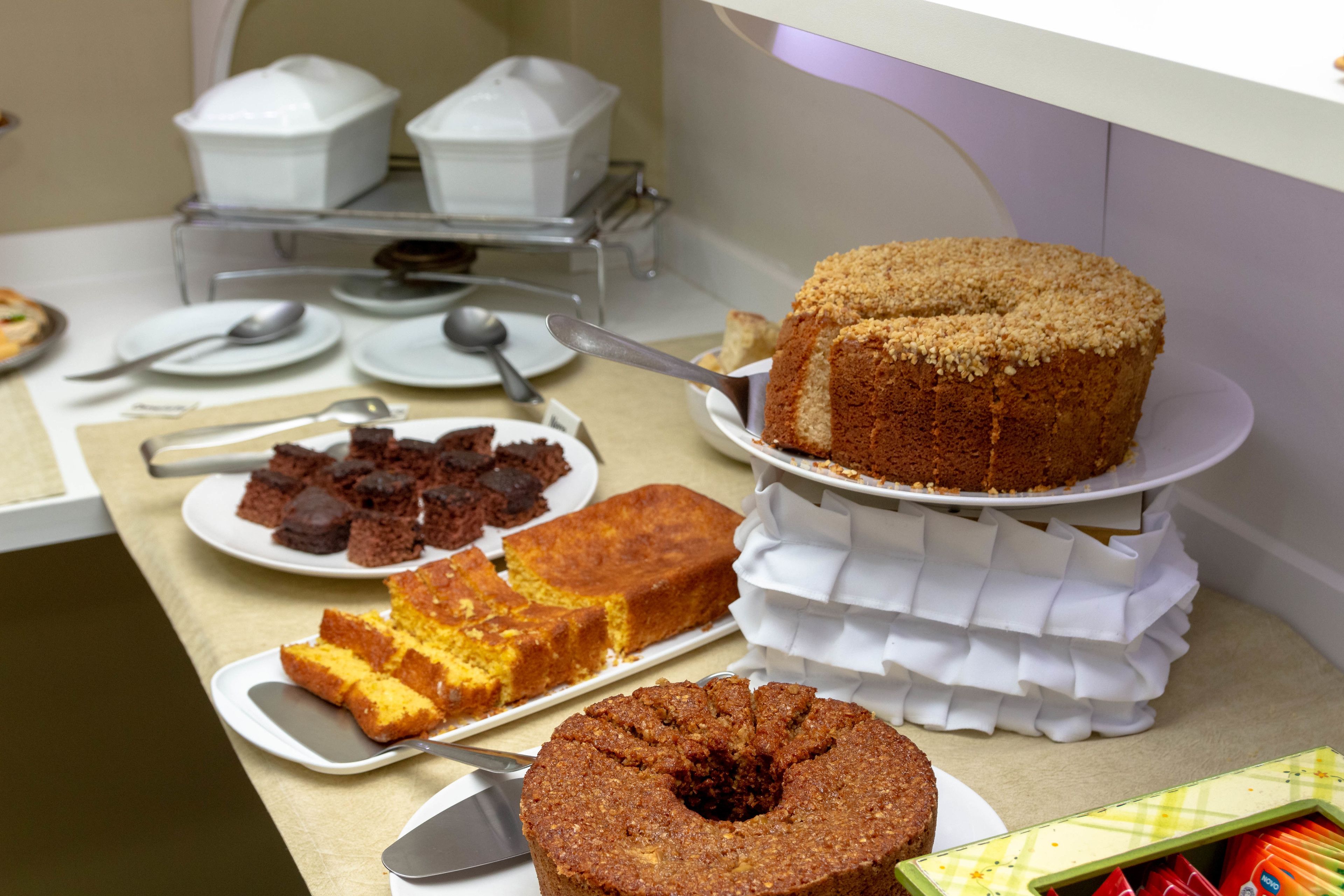 A buffet table with various cakes and desserts, including a bundt cake, a slice of yellow cake, and several brownies.