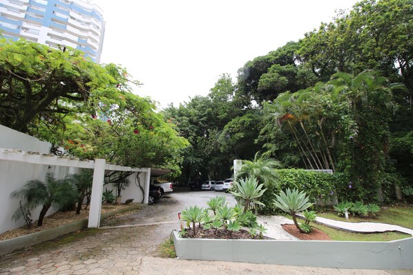 A courtyard with a white fence, various plants, and parked cars. - Hotel do Bosque (Balneário Camboriú)