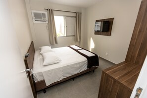 A neatly arranged hotel room with a bed, a wooden bedside table, a mounted TV, and a window with curtains. - Hotel do Bosque (Balneário Camboriú)