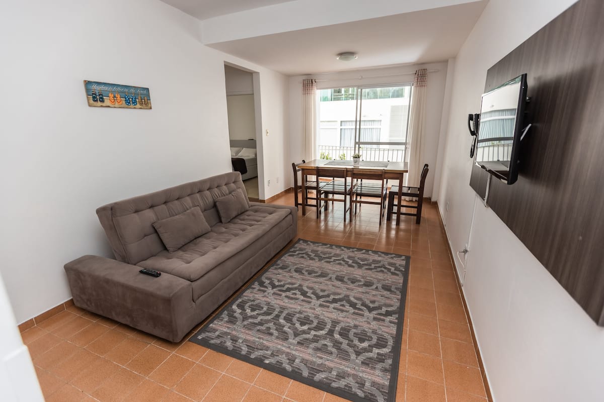 A living room with a sofa, a dining table, and a TV mounted on the wall.