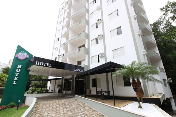 A hotel entrance with a sign, a covered outdoor seating area, and a palm tree. - Hotel do Bosque (Balneário Camboriú)