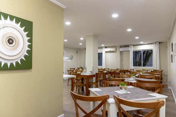 A dining area with multiple tables and chairs, a clock on the wall, and a large decorative piece on the left. - Hotel do Bosque (Balneário Camboriú)