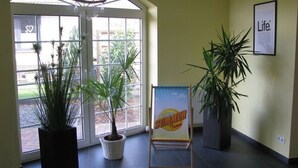 Zona de recepción con un gran puerta de cristal arqueada, plantas en macetas y un cartel sobre un atril.
