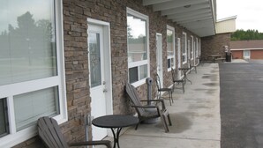 A row of outdoor seating with chairs and tables, a stone facade, and large windows. - Goodman's Motel (Baldwin)