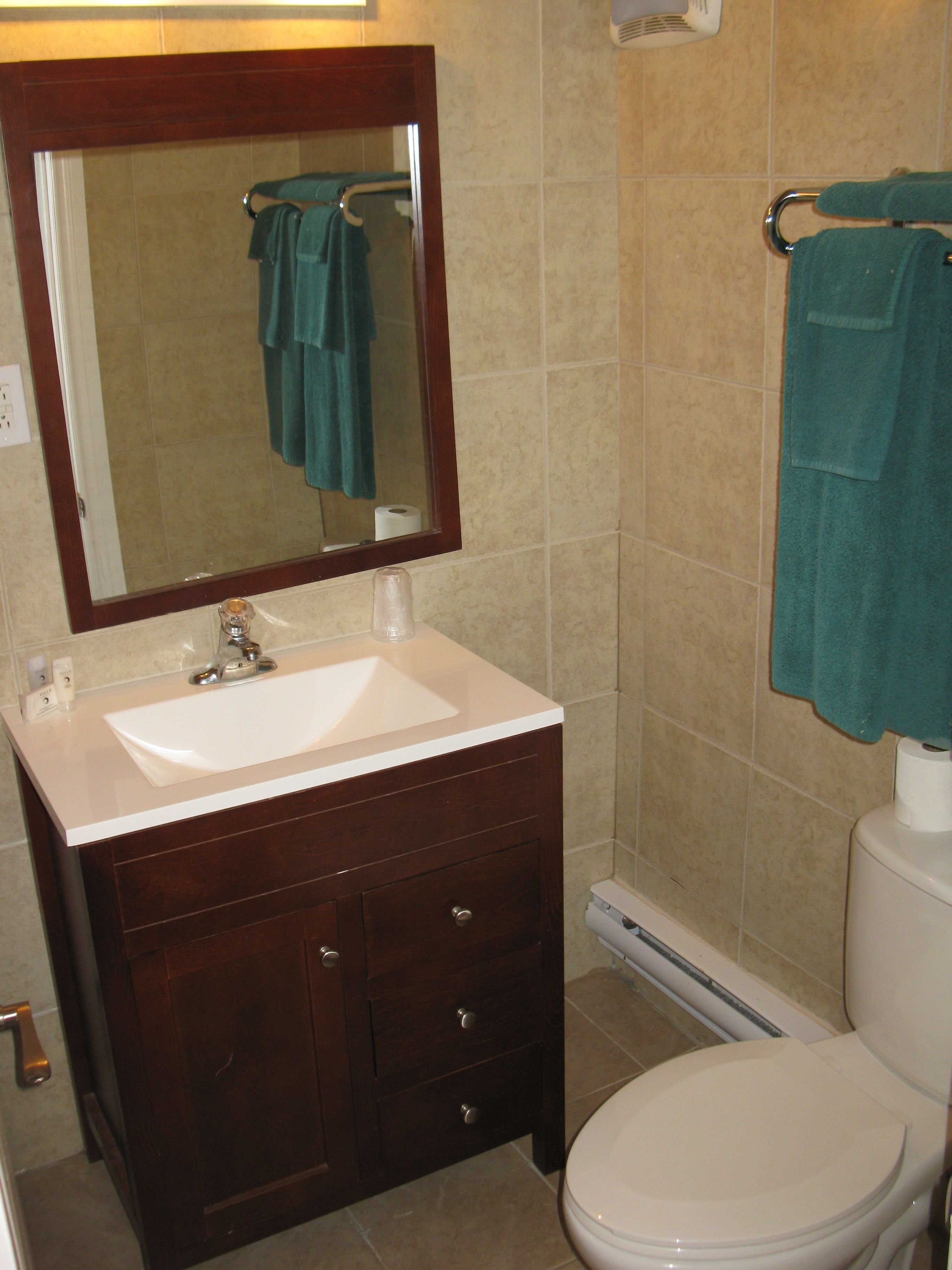 A bathroom with a white sink, dark wooden vanity, a mirror, a toilet, and two towels hanging on towel racks.